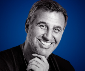 Marcelo Borlando, smiling confidently with his hand resting on his chin, against a blue background.