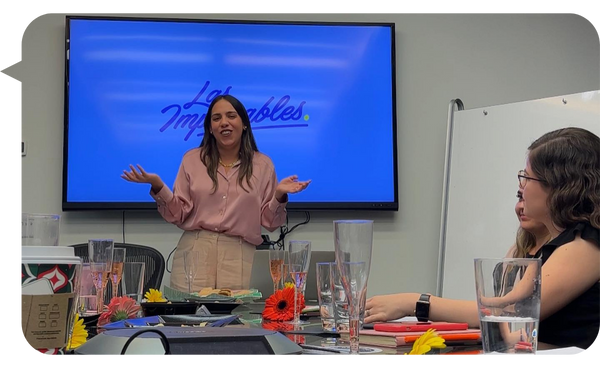 Alejandra Tejeda conducting a workshop, with the "The Unstoppable" logo on a screen behind her, engaging with participants seated around a table.